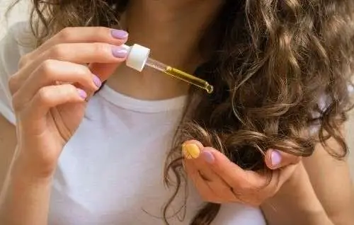 Frau tropf sich mit einer Pipette ein Haaröl für Locken auf ihr Haar