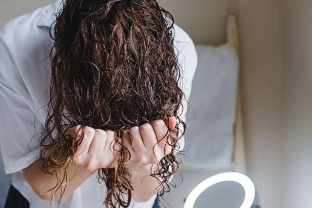 Naturlocken stylen: Frau stylt Locken kopfüber und knetet sie in Form
